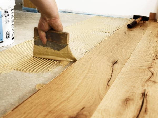 L'artisan carreleur de Strasbourg pose un parquet avec une brosse à colle.